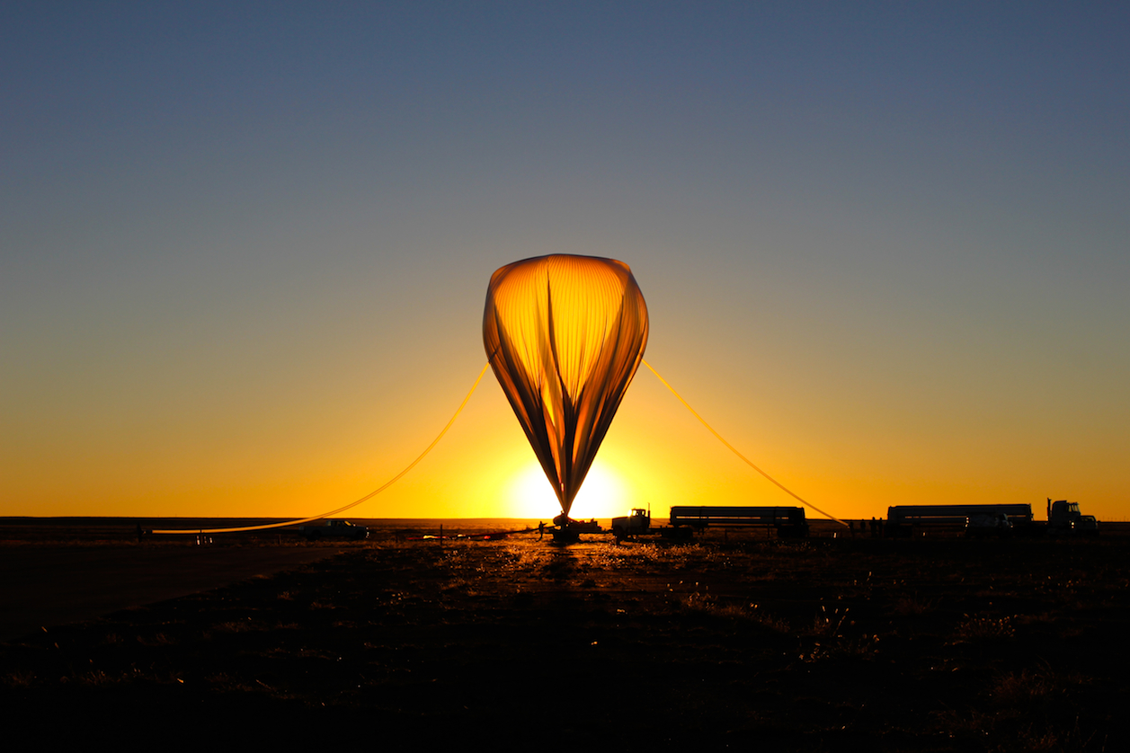 An inflated weather balloon with the Sun on the rise behind it